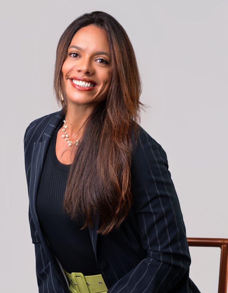 A advogada Vanessa Carrilho Rosa sorrindo, de blazer risca de giz, sentada com um livro sobre inventário e partilha